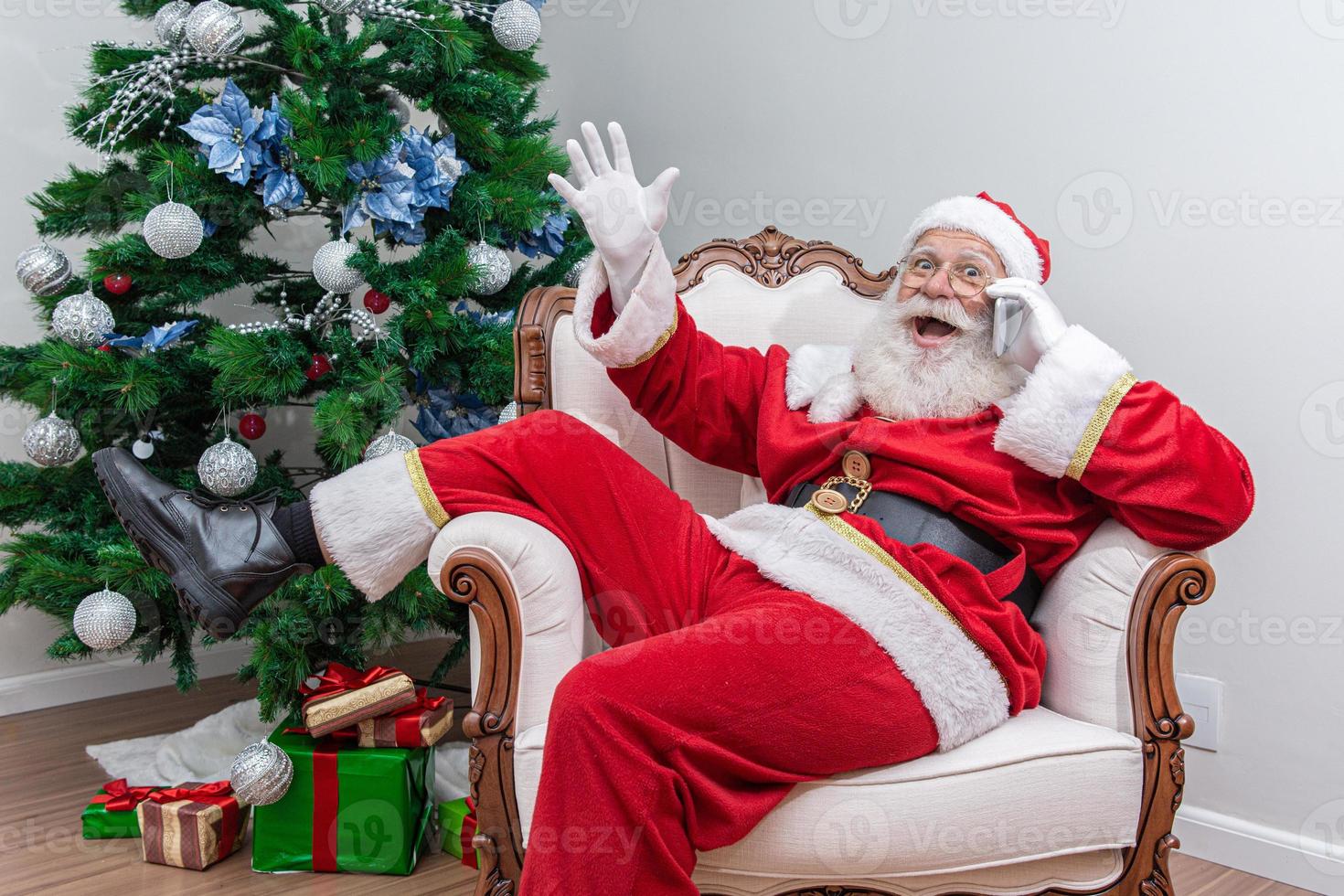 santa claus usando un teléfono inteligente. hablando por teléfono con un niño. analizando las solicitudes de navidad. foto