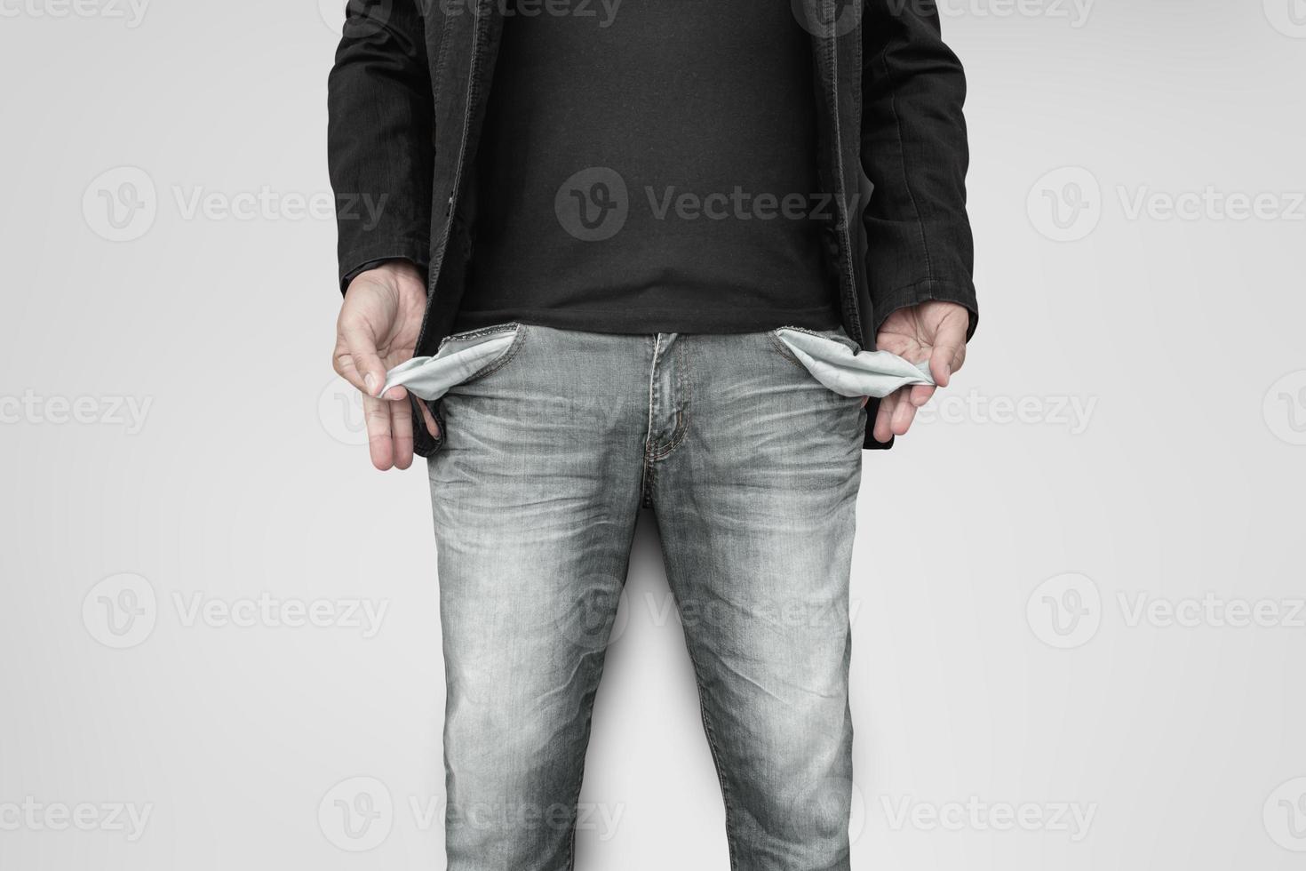 Man showing his empty pockets on gray wall background. photo