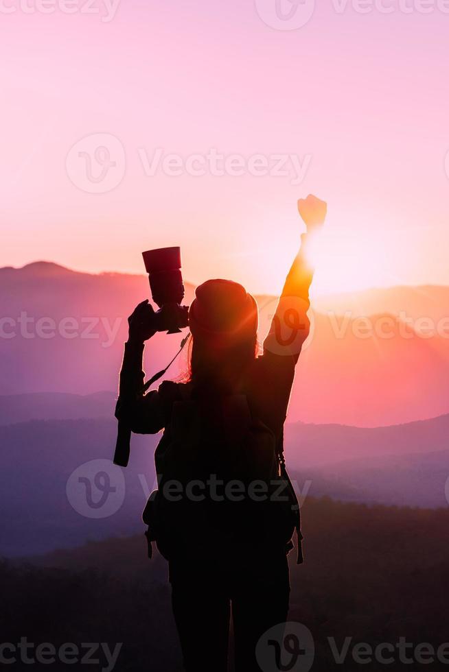 Young traveler woman raise hands up for her success with sunset on mountain natural background. photo