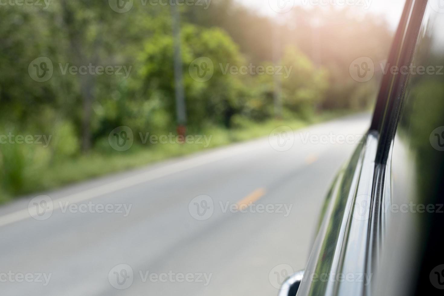 Abstract and blurred of beside car  on the road. View of beside to rear car can see blur of windows glass. And blurred of car driving on asphalt road with green grass and trees. Traval trip to nature. photo