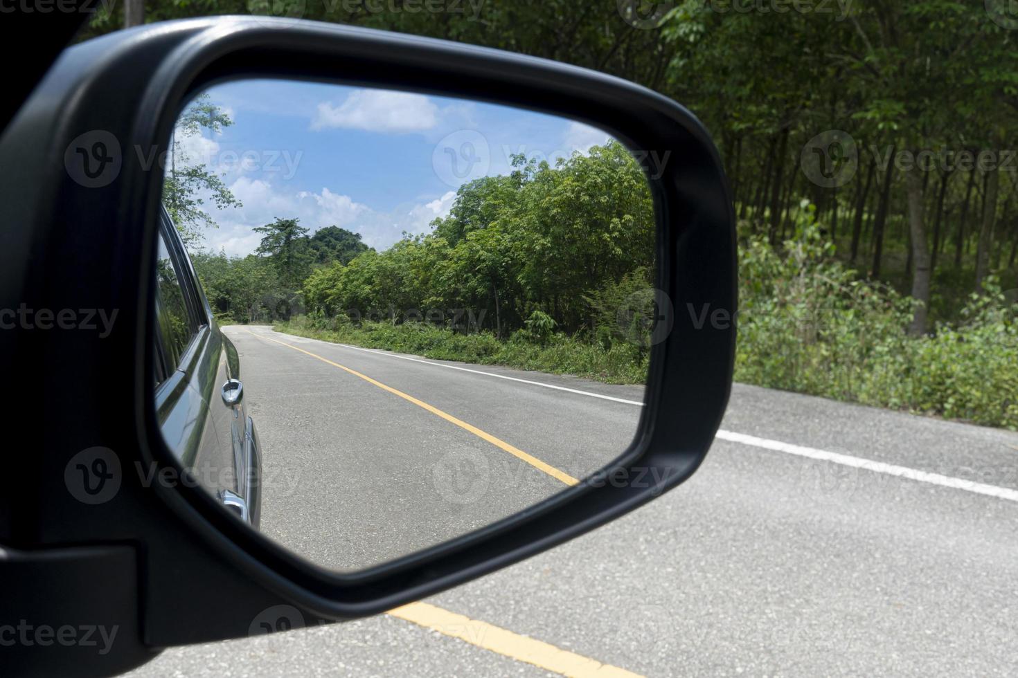 Vista interior del ala de los espejos. vista trasera de un coche gris con carretera asfaltada y árboles verdes durante el día. despejar el tráfico en las zonas rurales. foto