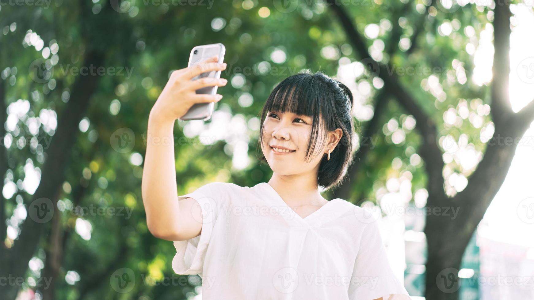 mujer soltera de negocios asiáticos adulta joven usando fondo de teléfono móvil con árbol verde borroso. foto