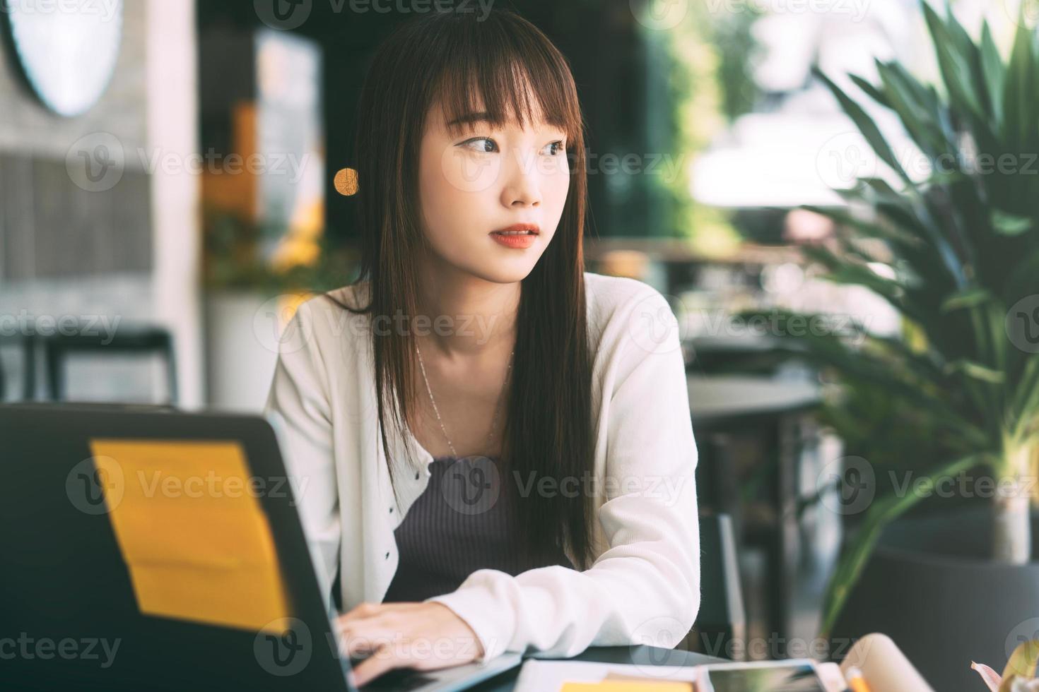 joven estudiante universitaria asiática adulta que usa una computadora portátil para estudiar y trabajar en línea en un café. foto