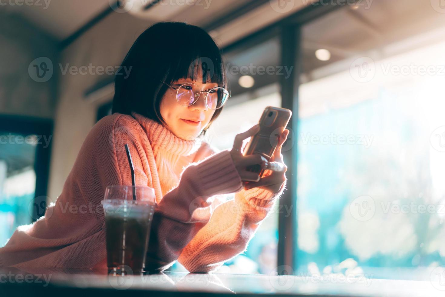 Young adult asian woman using mobile phone for social media background with window and warm sunlight on winter photo