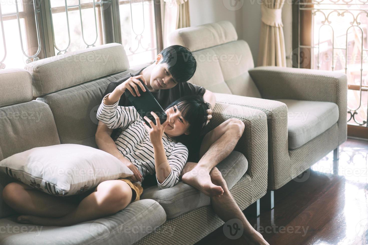 Young adult asian lover couple sitting on sofa and play game cozy style indoor on day. photo