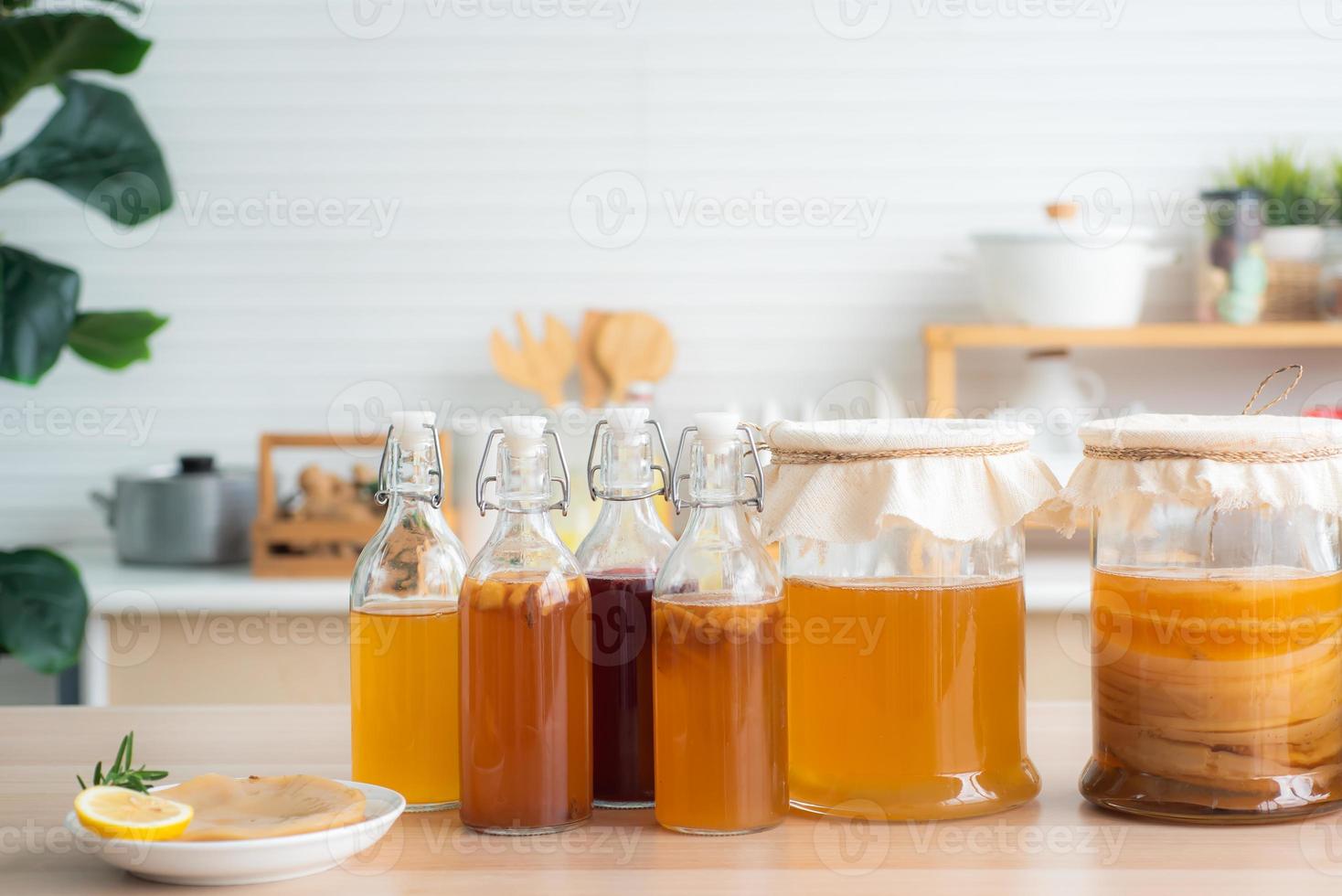 Homemade fermented raw kombucha tea, variety of flavors in bottles and glass jars mix with a fruit juice and scoby on wooden table. Healthy natural probiotic drink. photo