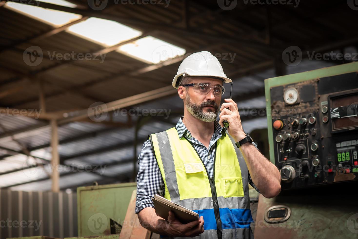 ingeniero o técnico caucásico con uniforme de seguridad están trabajando y revisando el plan de maquinaria de mantenimiento en tableta y hablando por walkie talkie en la fábrica industrial. foto