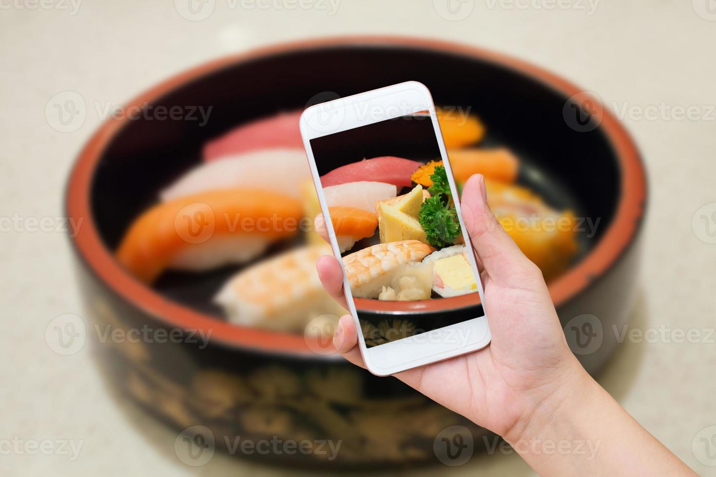 Female hand taking photo of sushi set with mobile phone