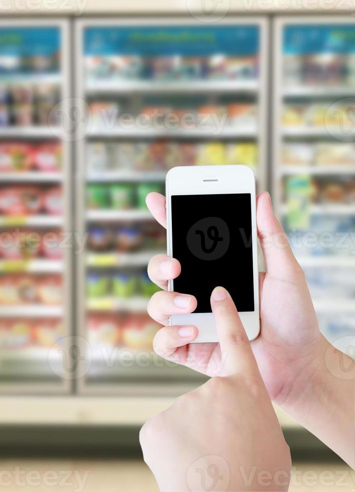 Female hand holding mobile smart phone on Supermarket blur background, business concept photo