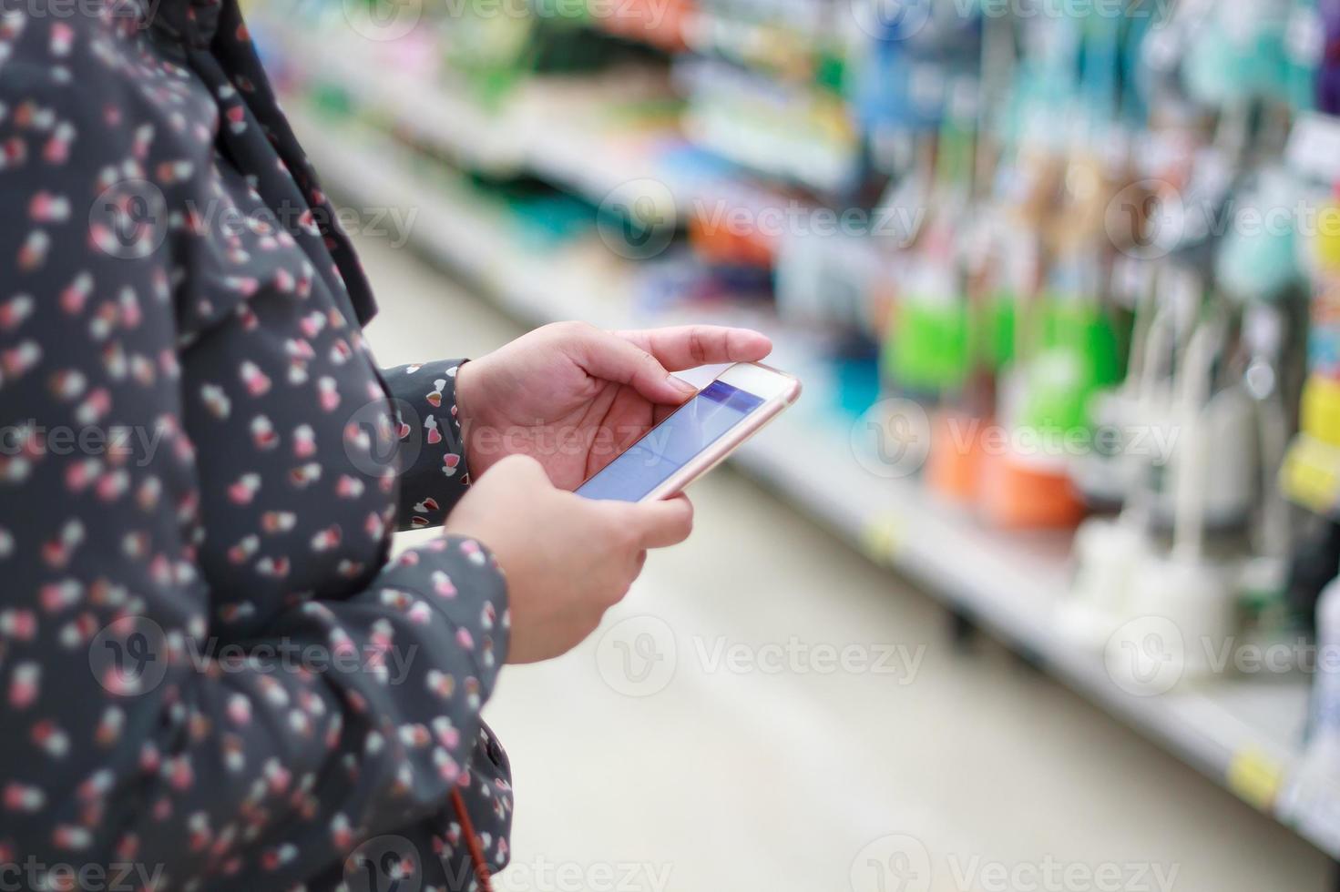 mujer que usa el teléfono móvil mientras compra en el supermercado foto