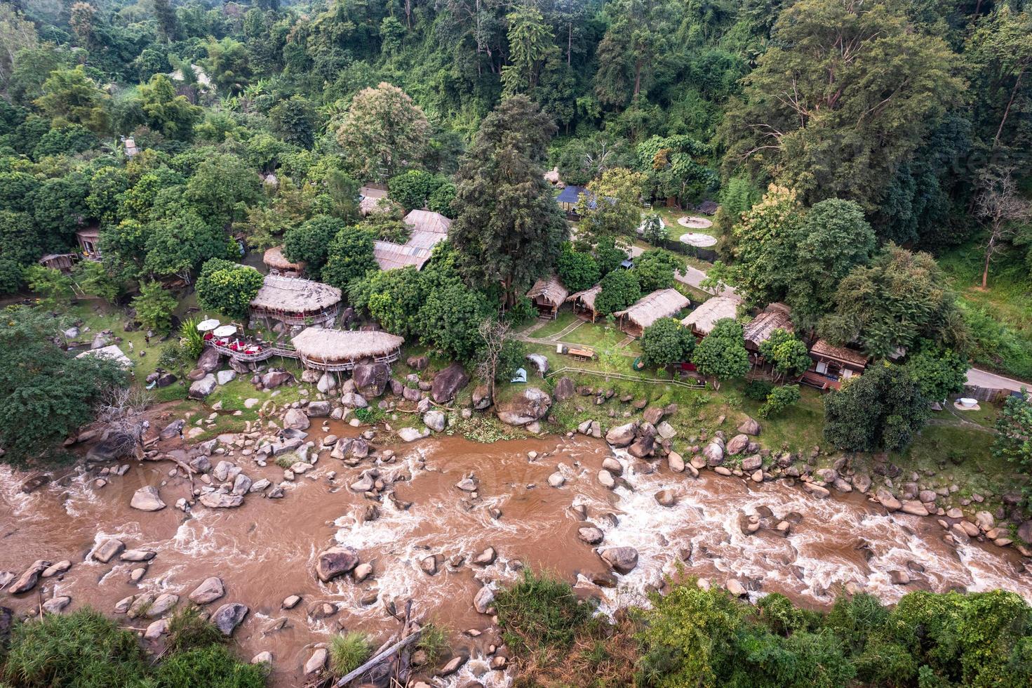 Aerial view of wooden bungalow in tropical rainforest with natural rapids in the valley photo