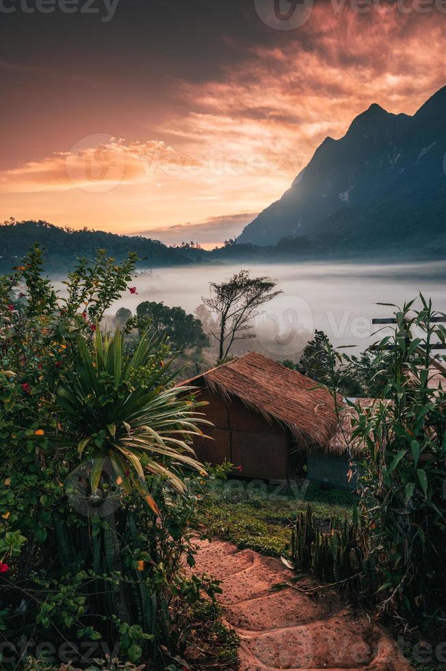 vista de la cabaña de madera con cielo colorido en la selva tropical y niebla que fluye en el valle en el campo foto