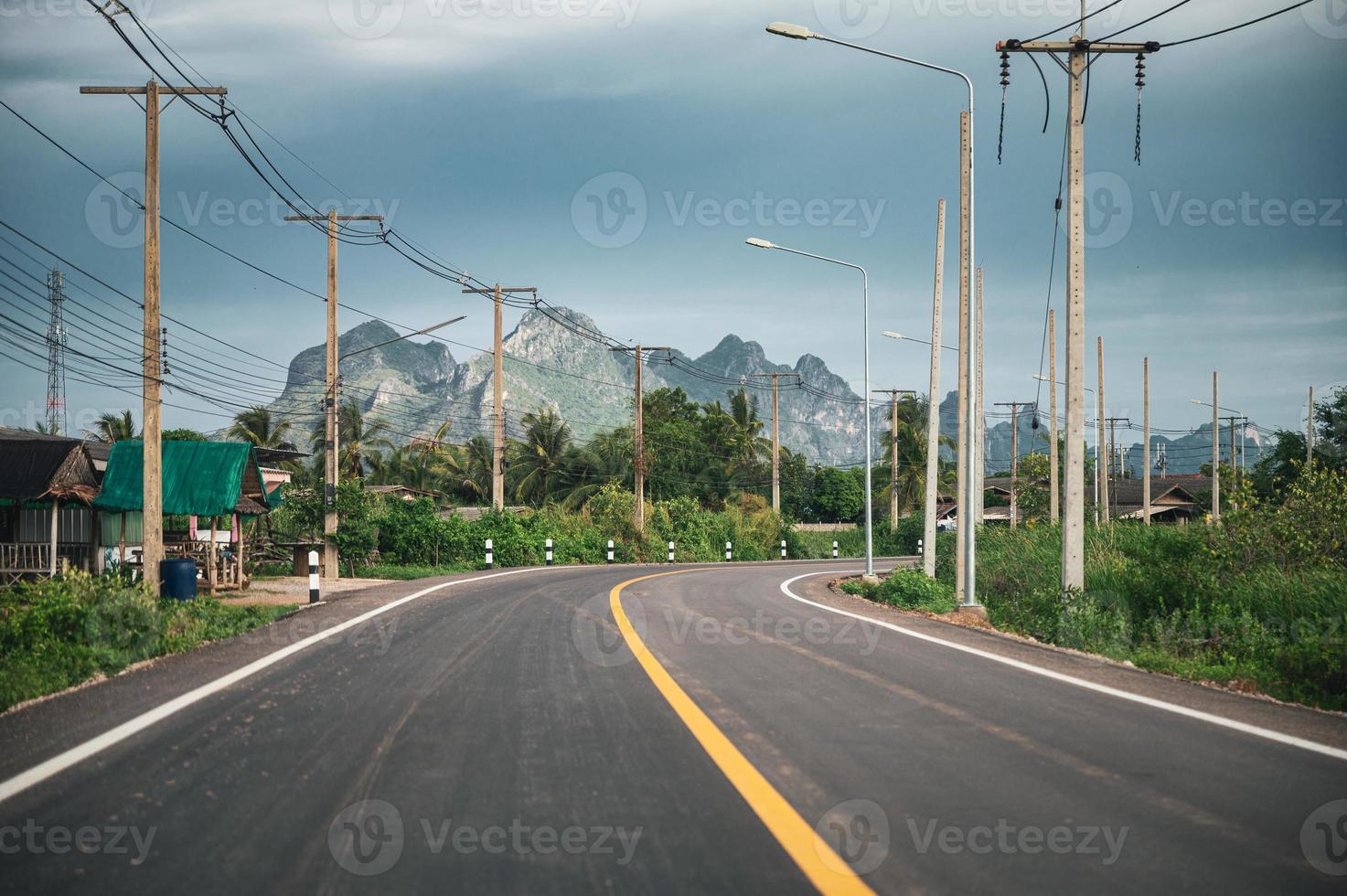 Asphalt road with mountain range and utility pole and lamppost in countryside at Sam Roi Yot photo