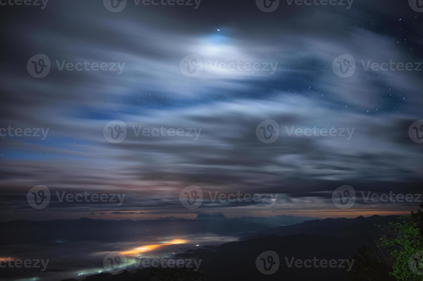 paisaje nublado que sopla a través del cielo azul con estrellas y luz de la luna sobre el pico de la montaña en el parque nacional por la noche foto