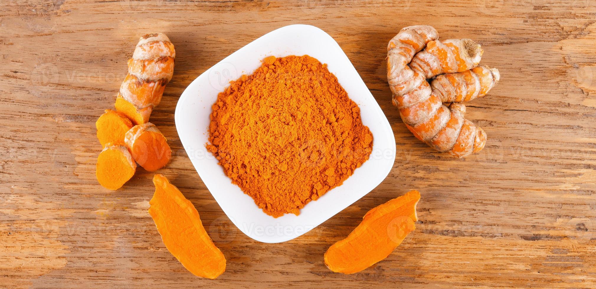 Turmeric roots with turmeric powder on wooden background photo