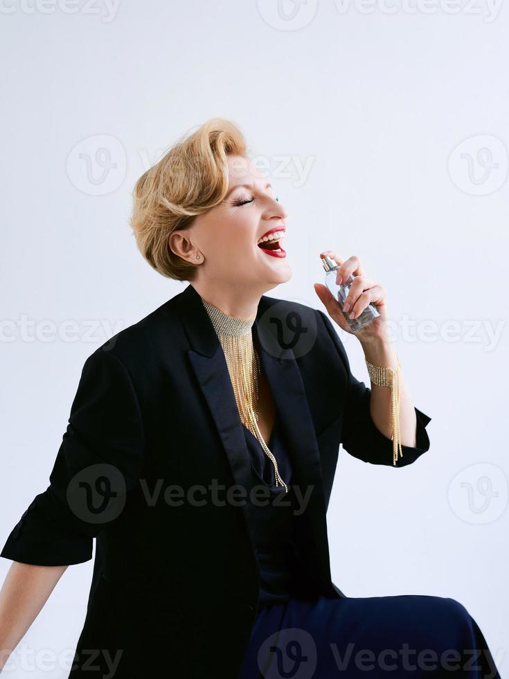 mujer madura de moda en esmoquin aplicando perfume. maquillaje, moda, concepto antienvejecimiento foto