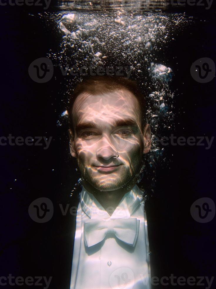 portrait of young man in bow tie and tail-coat underwater on the black background photo