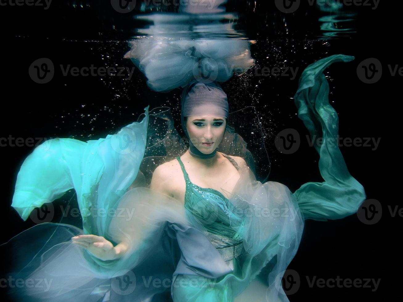 art portrait of the young beautiful woman in green dress on black background underwater in the swimming pool photo