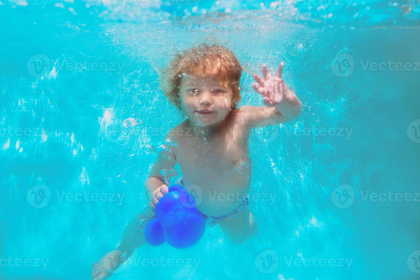 Cute smiling adorable baby girl diving underwater blue pool. Active lifestyle, child swimming lesson. Water sports activity during family summer vacation in tropical resort photo
