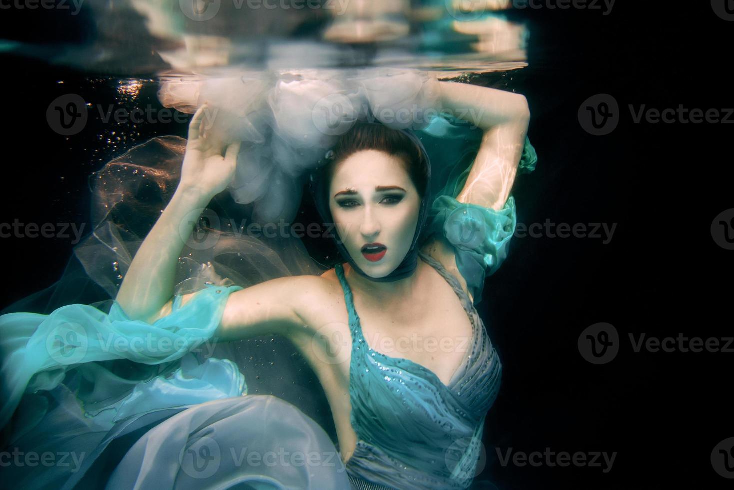 retrato artístico de la joven y hermosa mujer vestida de verde con fondo negro bajo el agua en la piscina foto