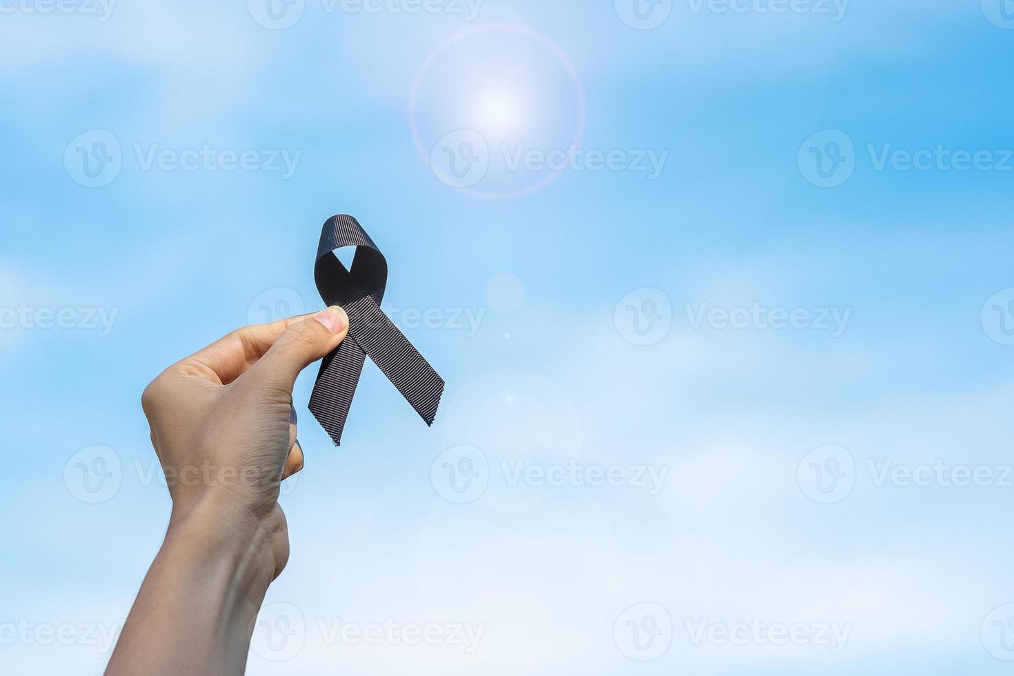 melanoma y cáncer de piel, mes de concientización sobre lesiones por vacunas y conceptos de descanso en paz. hombre que sostiene la cinta negra en el fondo del cielo foto