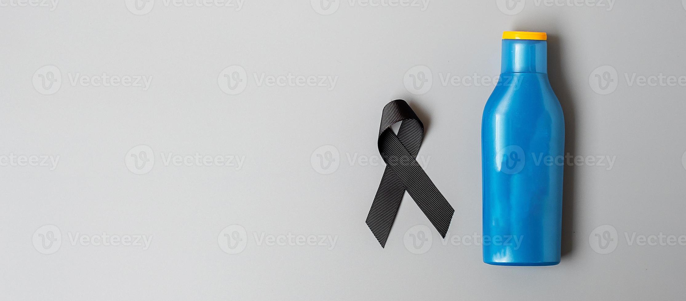 Melanoma and skin cancer awareness month. black Ribbon and body sunscreen bottle on grey background. World cancer day concept photo