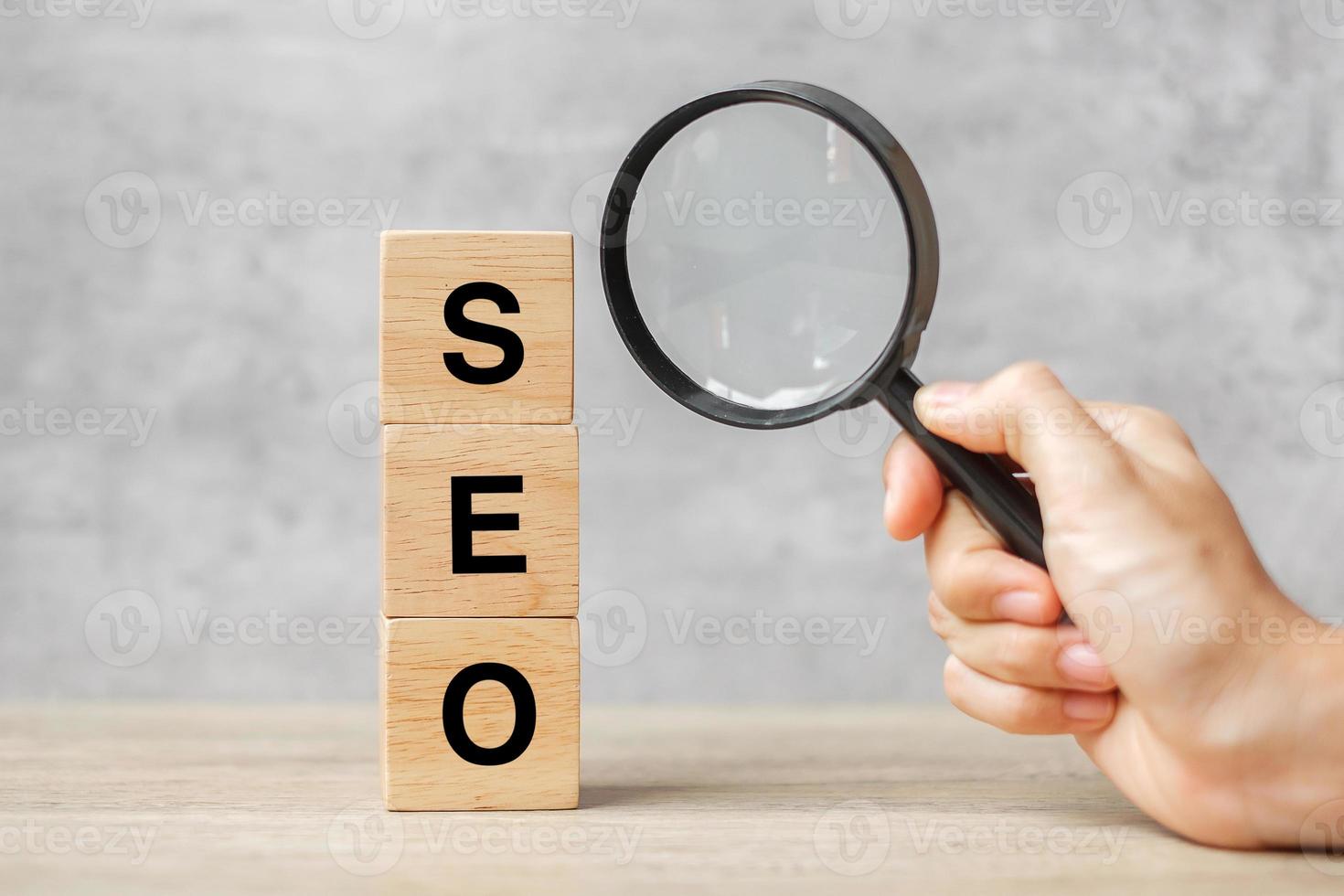 SEO Search Engine Optimization text wooden cube blocks and hand holding magnifying glass on table. Idea, Strategy, advertising, marketing, Keyword and Content concept photo