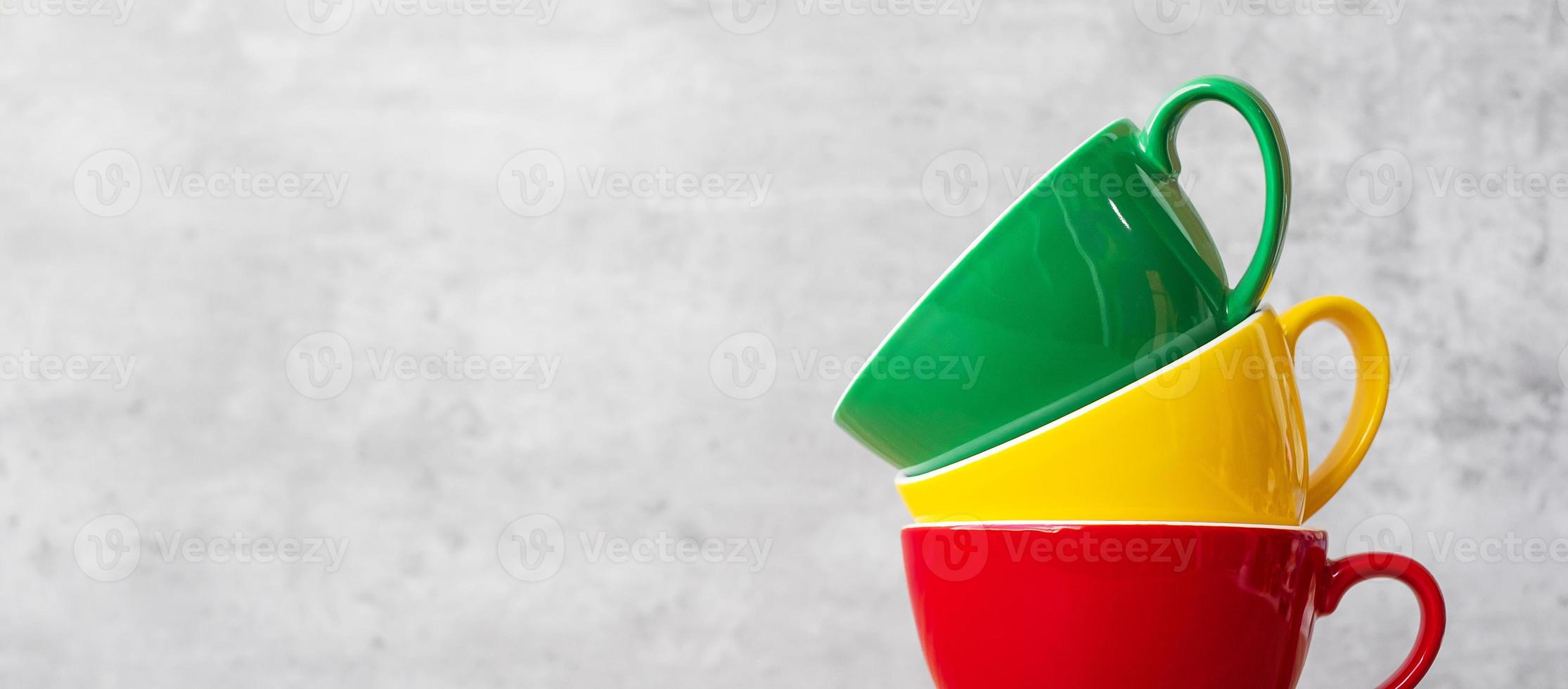 pila de coloridas tazas de café en el fondo de la pared en el café. taza de cerámica de color verde, amarillo y rojo en la mesa en casa. concepto del día internacional del café foto