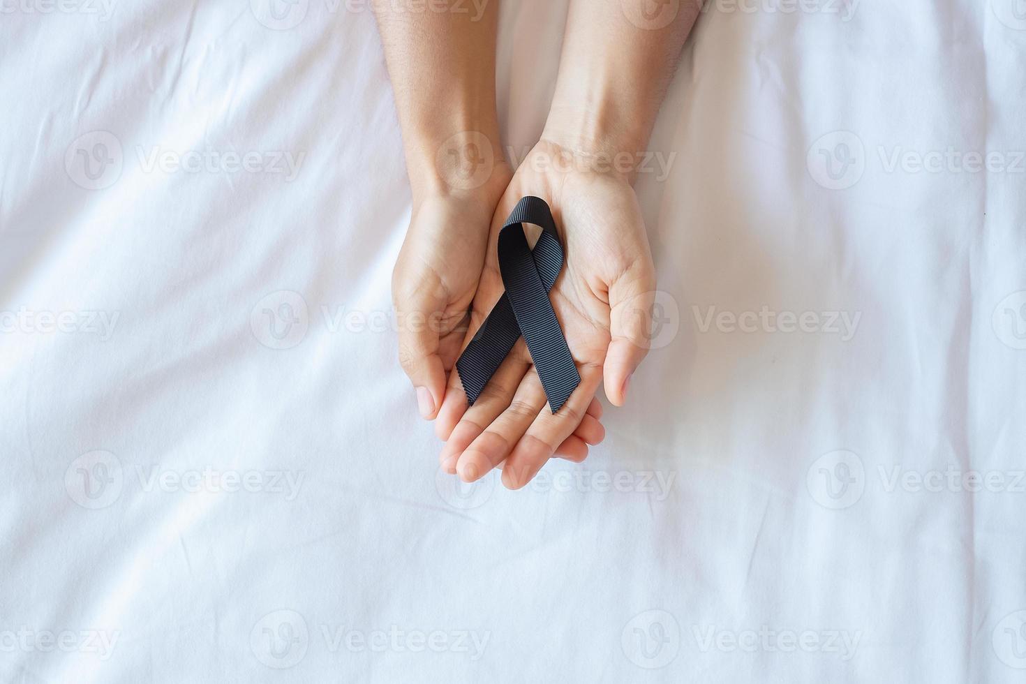 Melanoma and skin cancer, Vaccine injury awareness month and rest in peace concepts. Man holding black Ribbon on white bed background photo