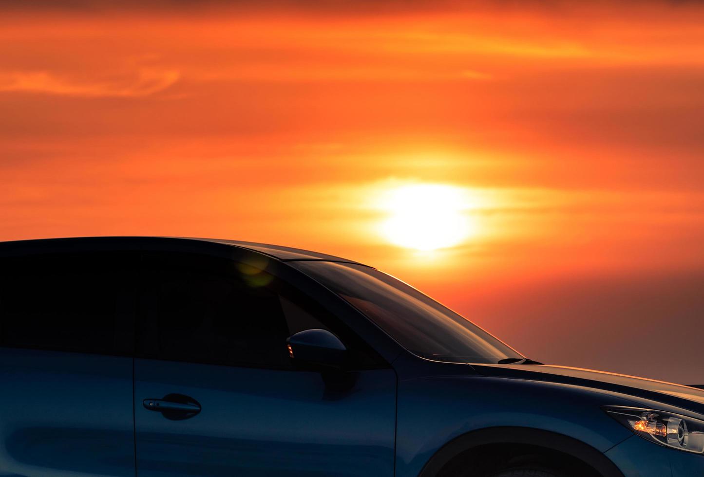 Side view of blue SUV car with sport and modern design parked on concrete road by sea beach at sunset. Electric car technology. Road trip travel. Automotive industry. Red and yellow sunset sky. photo