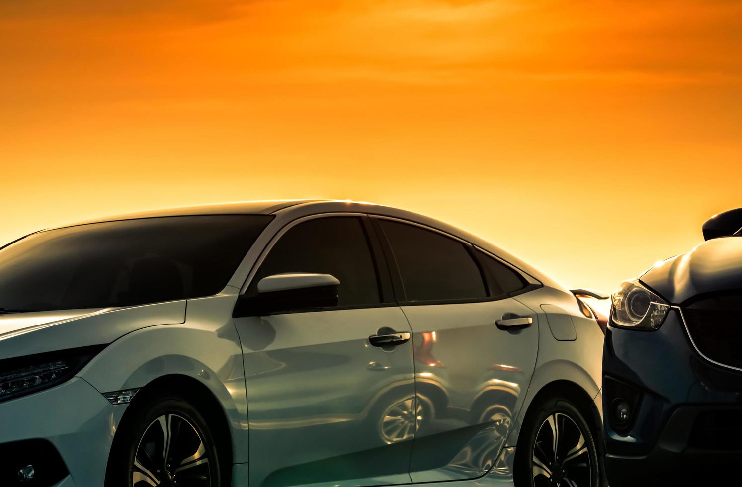 Front view of white car with luxury and modern design parked at parking lot with beautiful orange and golden sunset sky. Automotive industry. Road trip travel.  Shiny white car background for car care photo