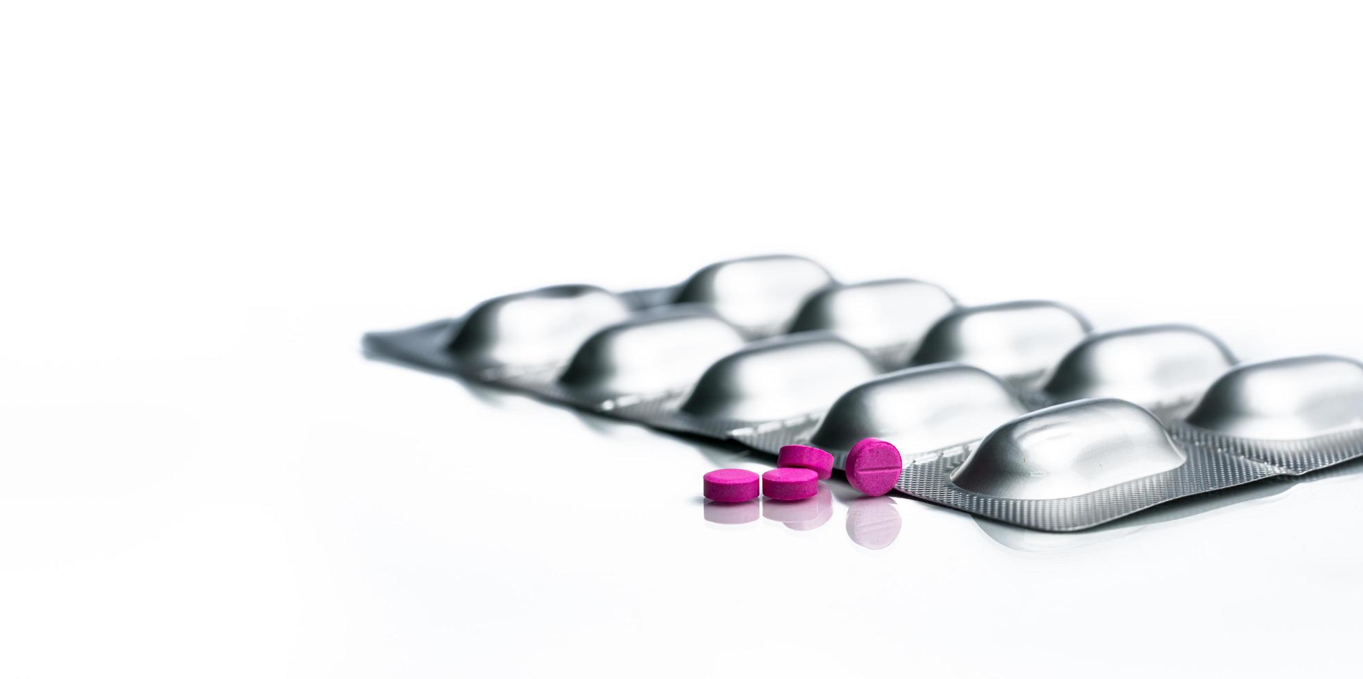 Macro shot of small pink tablets pills and silver aluminium foil blister pack of pills on white background. Pharmaceutical industry. Pharmacy  drug store. Global healthcare. Drug interactions concept. photo