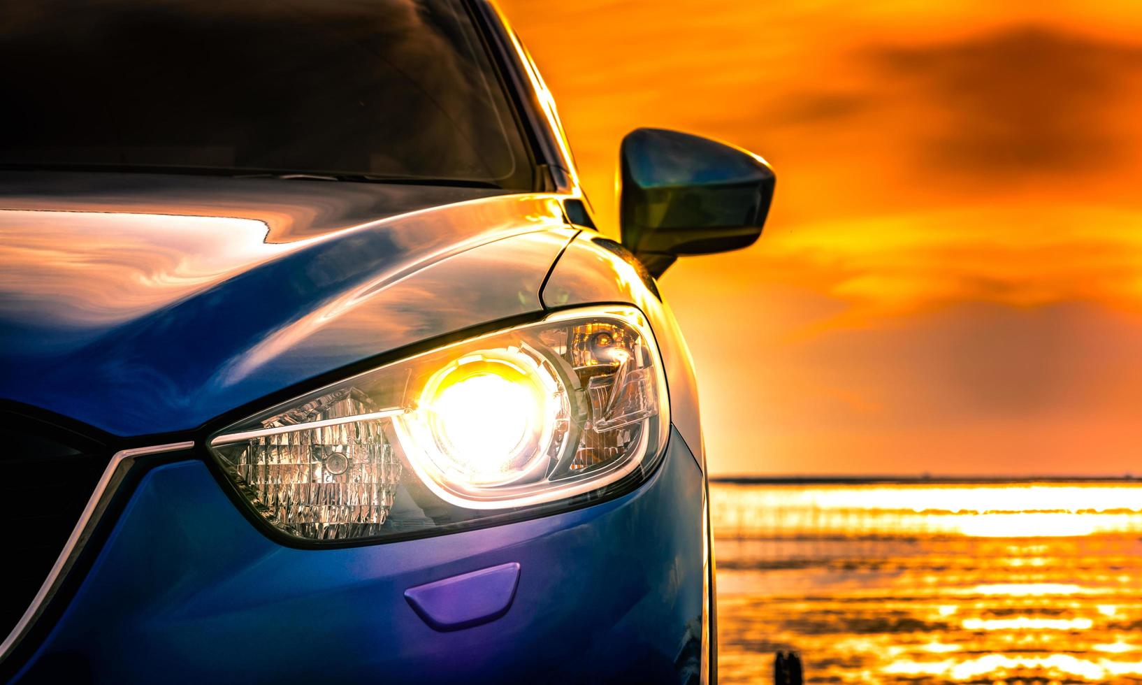 Blue compact SUV car with sport and modern design parked on concrete road by the sea at sunset. Environmentally friendly technology. Business success concept. Car with open headlamp light. photo