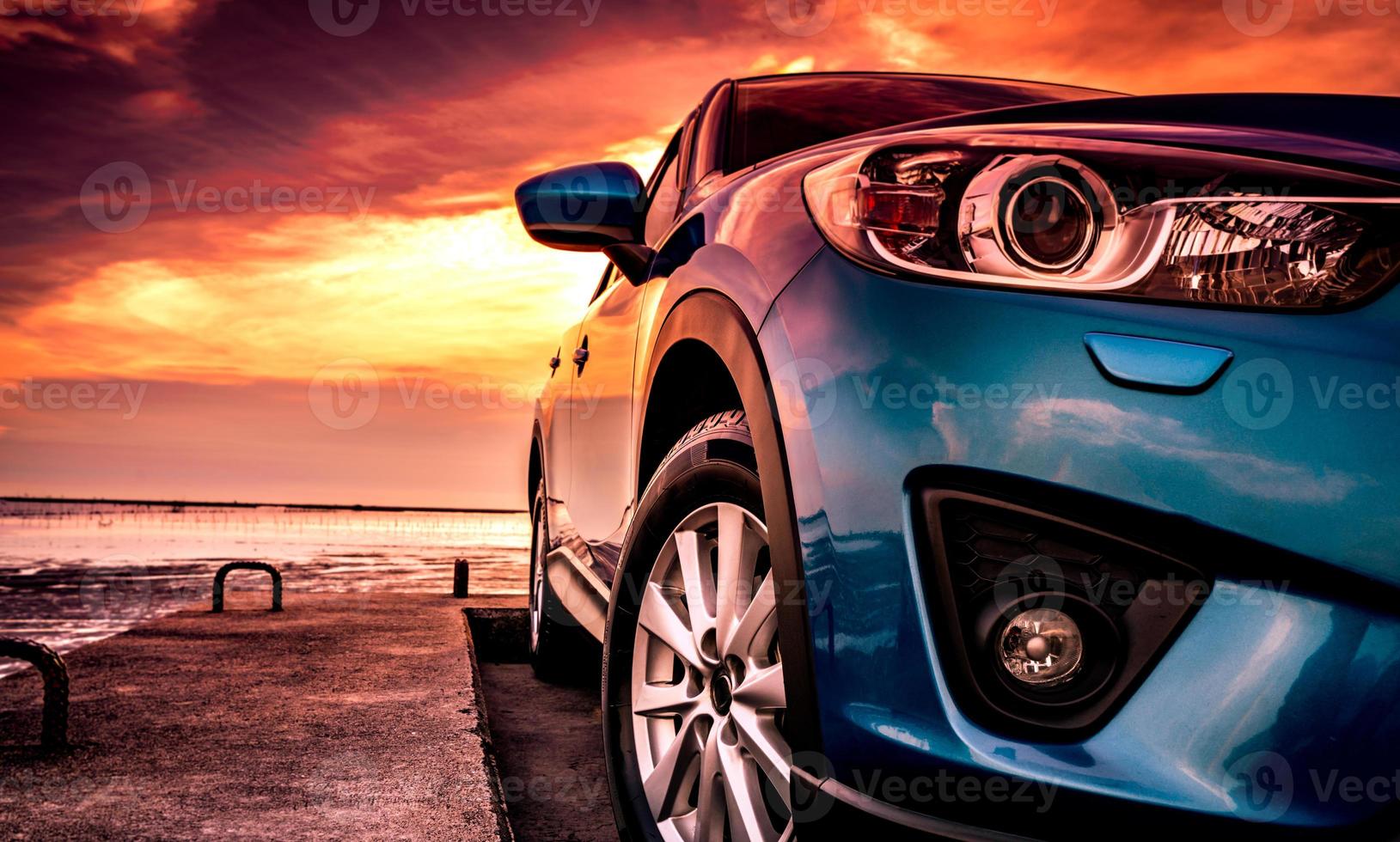 Blue compact SUV car with sport, modern, and luxury design parked on concrete road by the sea at sunset. Front view of beautiful hybrid car. Driving with confidence. Travel on vacation at the beach. photo