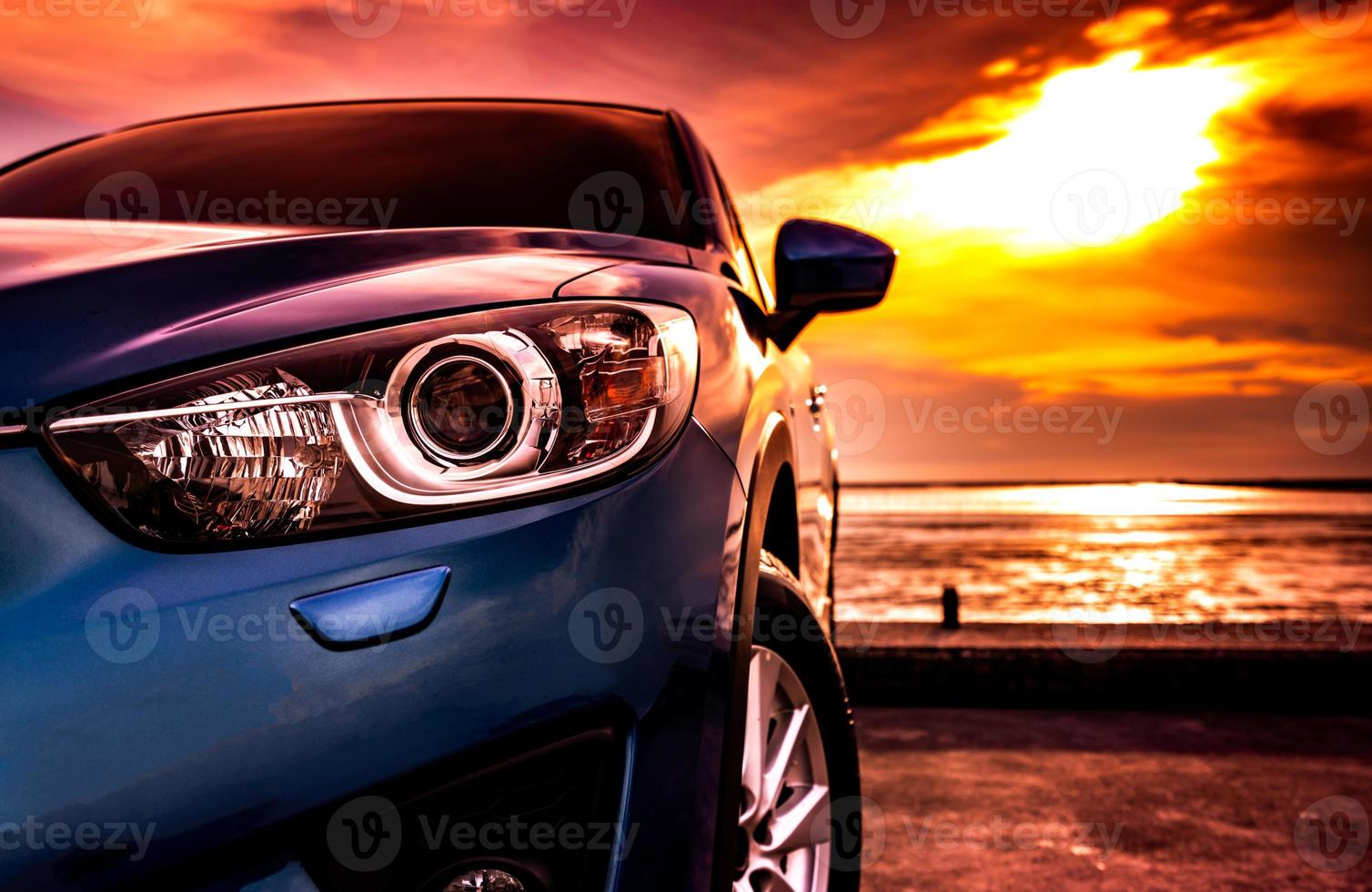 Blue compact SUV car with sport, modern, and luxury design parked on concrete road by the sea at sunset. Front view of beautiful hybrid car. Driving with confidence. Travel on vacation at the beach. photo