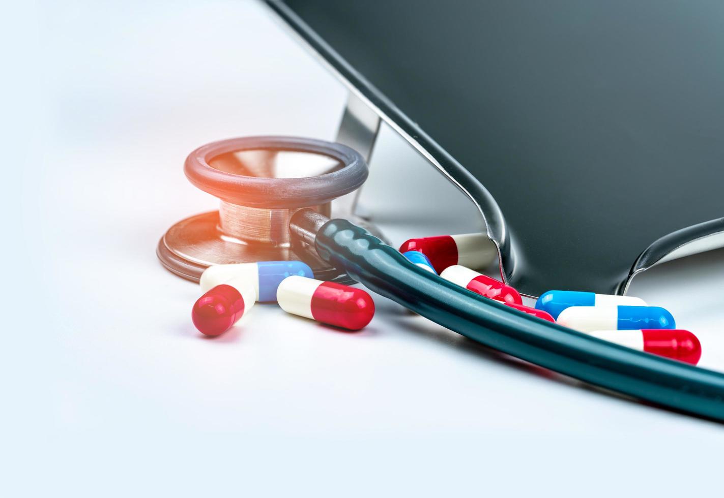 Green stethoscope with pile of antibiotic capsule pills on white table near drug tray. Antimicrobial drug resistance and overuse. Medical equipment for doctor. Clinical Cardiology concept. Health care photo