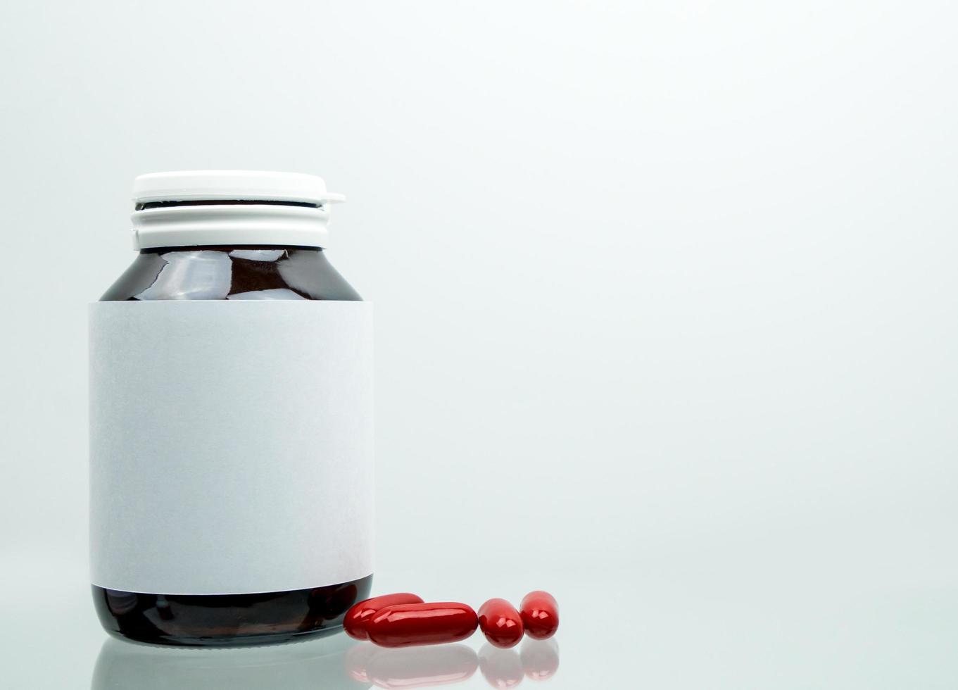 Macro shot of red multivitamins capsule pills for pregnant woman with amber bottle and blank label and copy space isolated on white background. Vitamin and supplement for pregnancy and elderly people. photo