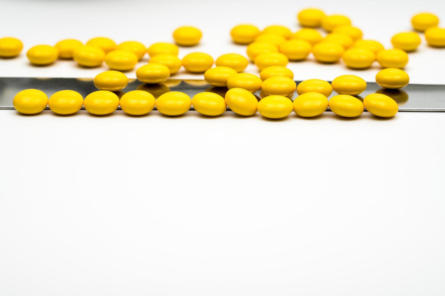 Macro shot detail of yellow round sugar coated tablets pills and stainless steel spatula on white background with copy space photo