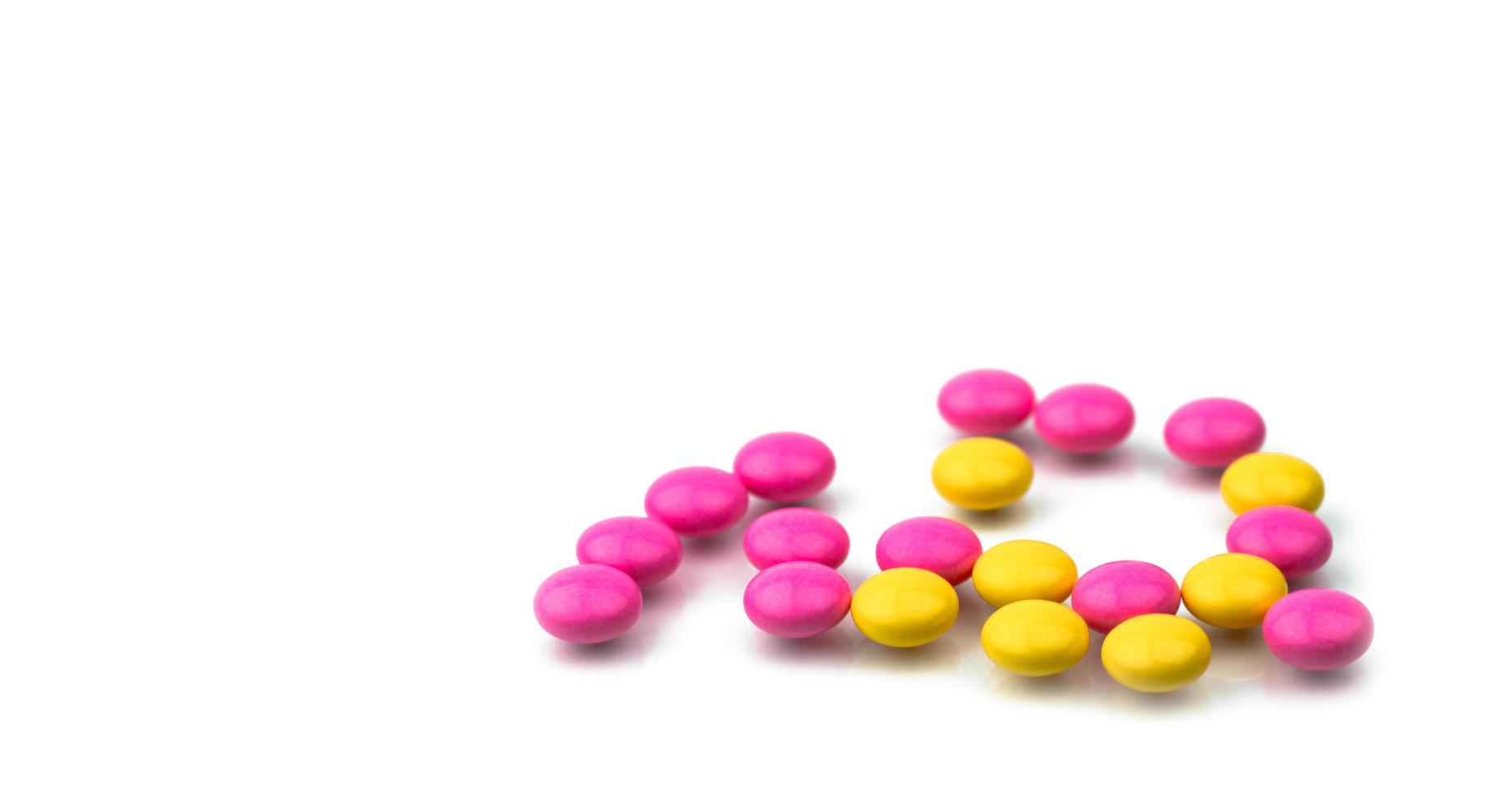 Pile of pink and yellow round sugar coated tablets pills isolated on white background with copy space. Colorful pills for treatment anti-anxiety, antidepressant and migraine headache prophylaxis. photo