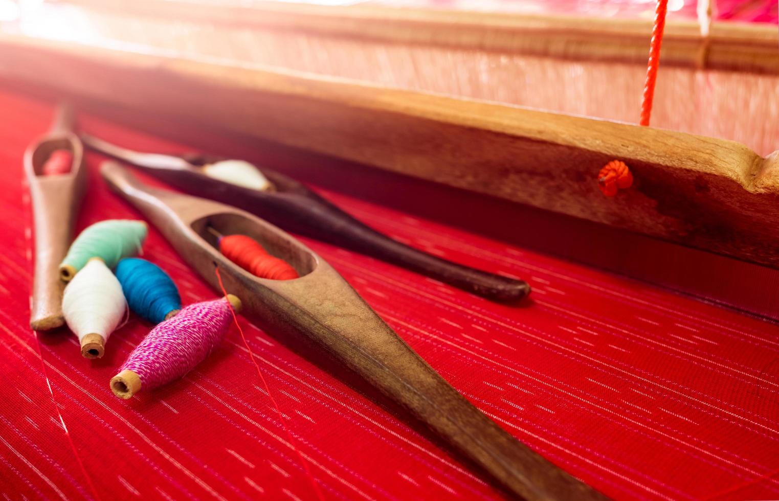 Selective focus on green, pink, blue, white yarn in weaving shuttle tool on weaving machine. Textile fabric weave. Weaving using traditional weaving loom and shuttle. Textile or cloth production. photo