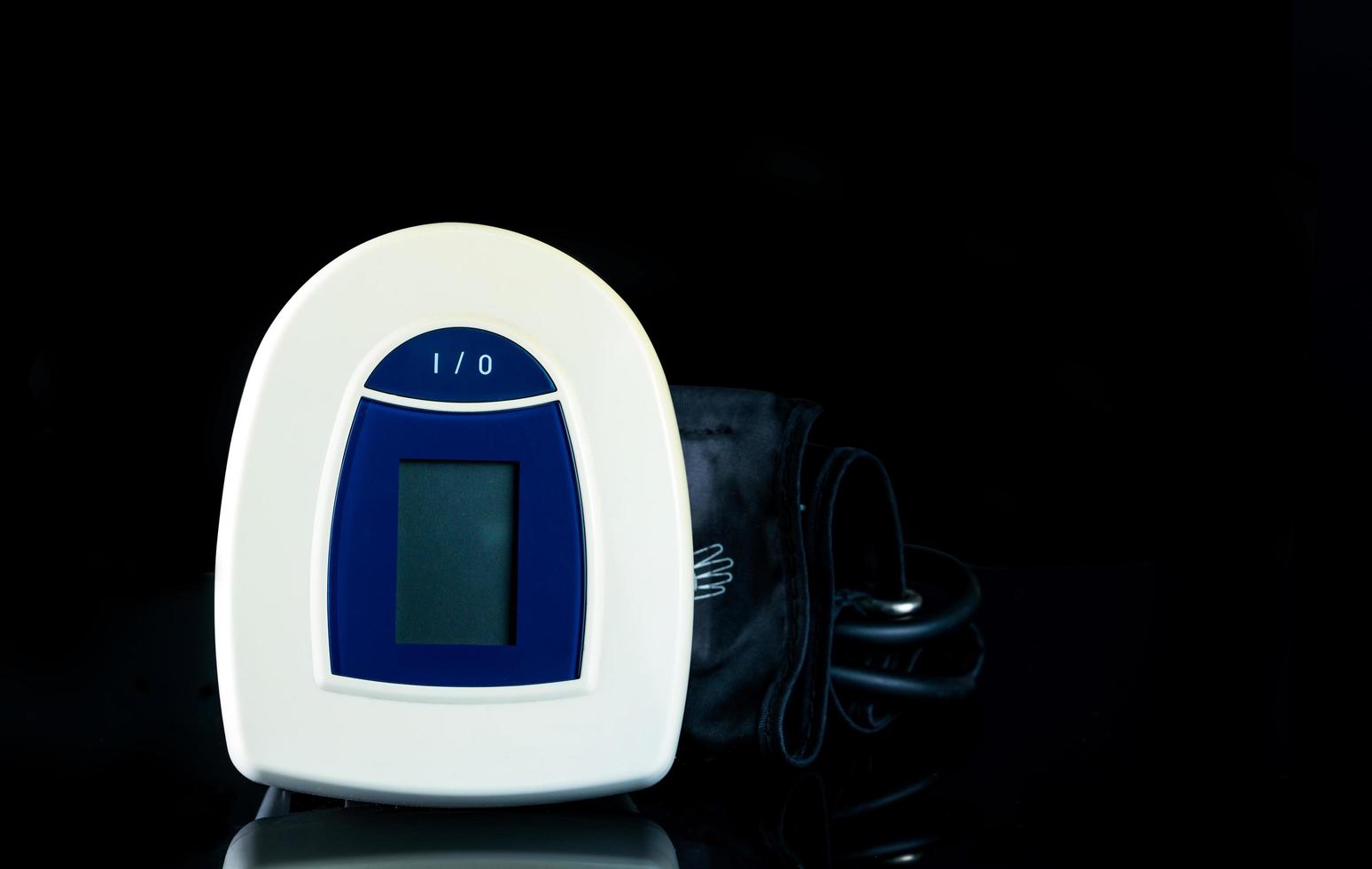 Blue-white digital blood pressure monitor with wide range cuff isolated on dark background. Health checkup concept photo
