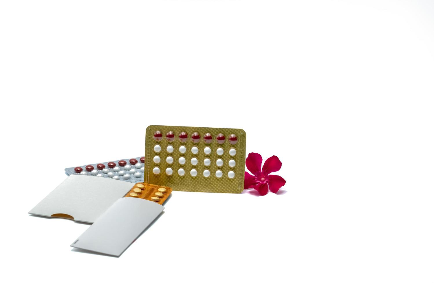 Contraceptive pills or birth control pills with pink flower on white background with copy space. Hormone for contraception. Family planning concept. White and red round hormone tablets in blister pack photo