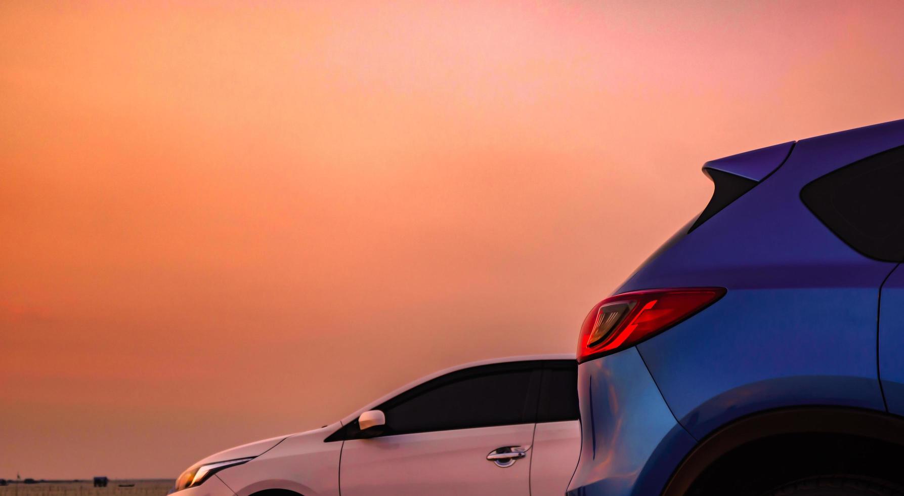 Blue compact SUV car with sport and modern design parked on concrete road by the sea at sunset. White Eco car. Environmentally friendly technology. Business success concept. photo