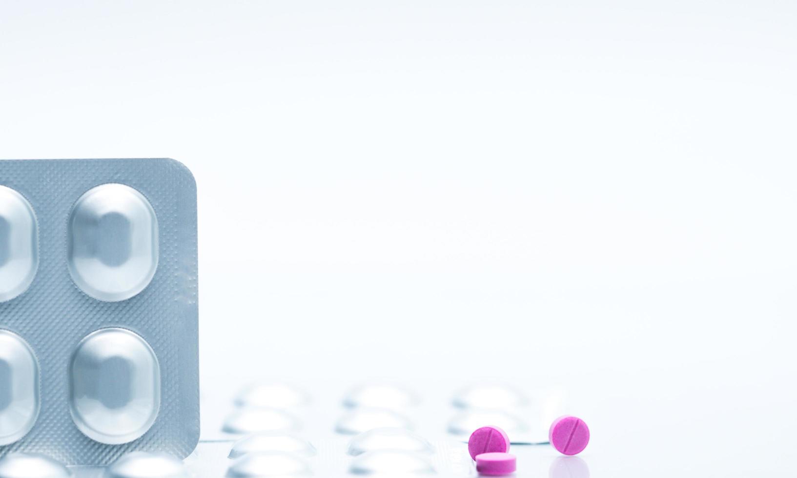 Macro shot of small pink tablets pills and silver aluminium foil blister pack of pills on white background. Pharmaceutical industry. Pharmacy  drug store. Global healthcare. Drug interactions concept. photo