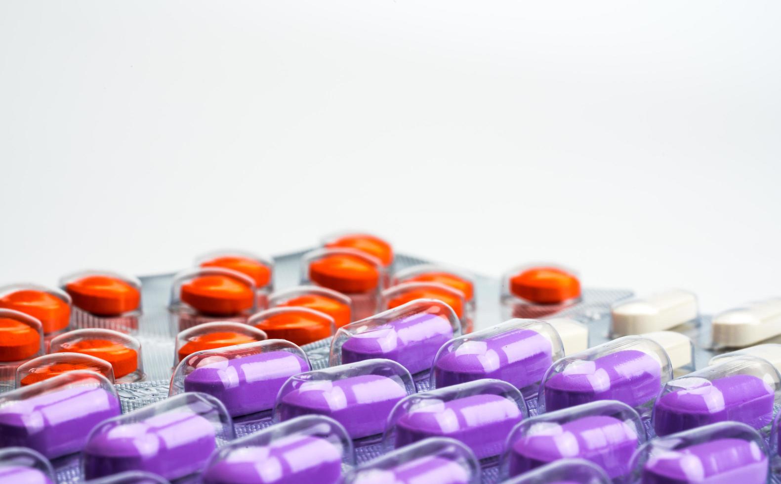 Macro shot detail of orange, purple and white tablets pills in blister pack on white background. Colorful medicine for relieve pain. NSAIDs drug for anti-inflammation can cause gastric ulcer. photo