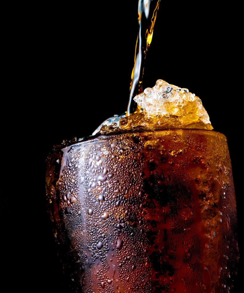 refresco que se vierte en un vaso con hielo aislado en un fondo oscuro con un camino de recorte y espacio para copiar. hay una gota de agua en la superficie de vidrio transparente. foto