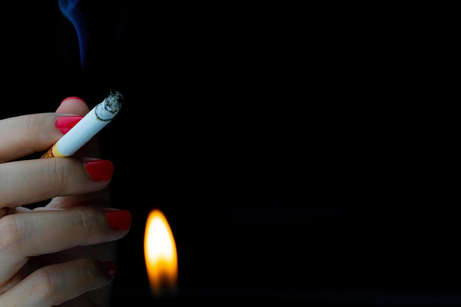 mujer sexy con uñas rojas está fumando cigarrillos en un fondo oscuro con espacio para copiar. dejar de fumar concepto. cigarrillo ardiendo con llama del encendedor. adicto a la nicotina 31 de mayo día mundial sin tabaco. foto
