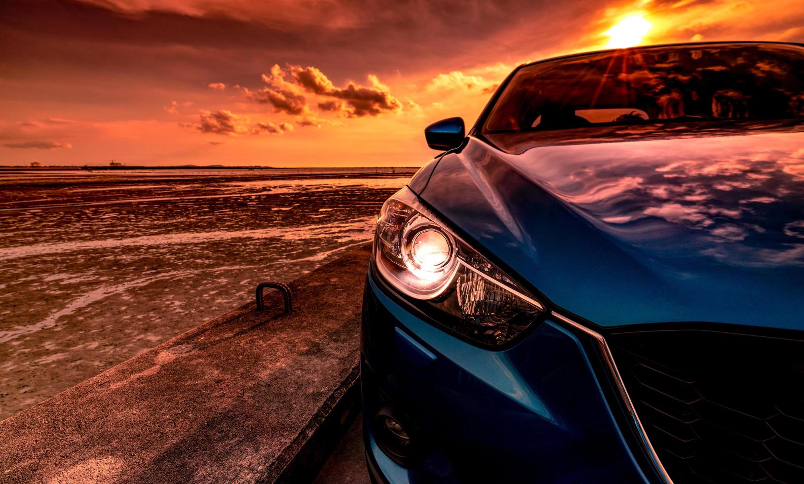 camión suv compacto azul con diseño deportivo y moderno estacionado en una carretera de hormigón junto al mar al atardecer. tecnología respetuosa con el medio ambiente. concepto de éxito empresarial. coche con luz de faro abierta. foto