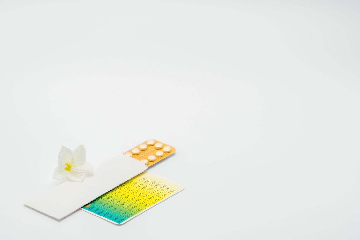 Birth control pills or contraceptive pill with paper case and white flower on white background. Family planning concept. Hormone replacement therapy. Hormonal acne treatment with anti-androgenic pill. photo