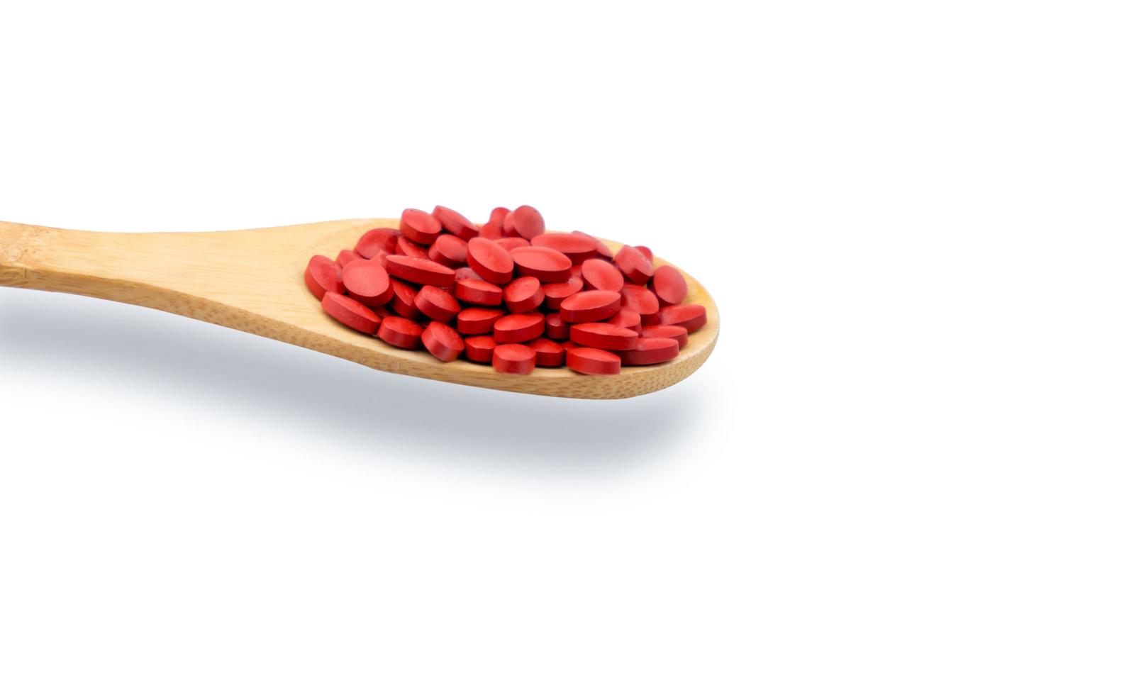 Iron tablets in spoon isolated on white background. Ferrous fumarate for treatment anemia in adult, elderly people and children. Blood donations concept. Red tablets pills on wooden spoon. Pharmacy photo